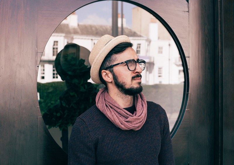 a man wearing a hat scarf and glasses stands in front of a window in richmond, _man with circular window 4k