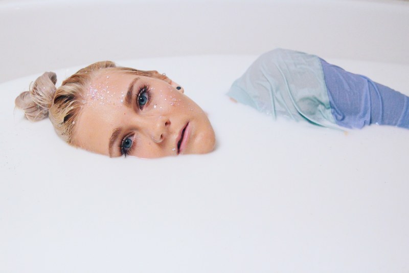 artistic portrait of a woman covered in glitter bathing in milk, milk bath 4k