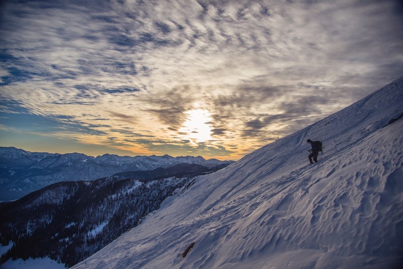 a man with mountaineering gear climbing down a snowy slope in the high mountains, climbing down a snowy slope at dusk 4k