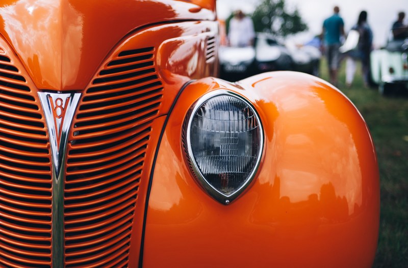 macro shot of the orange oldtimer vintage car front grill and left chrome headlight in knebworth house, macro of vintage grille and headlight 4k