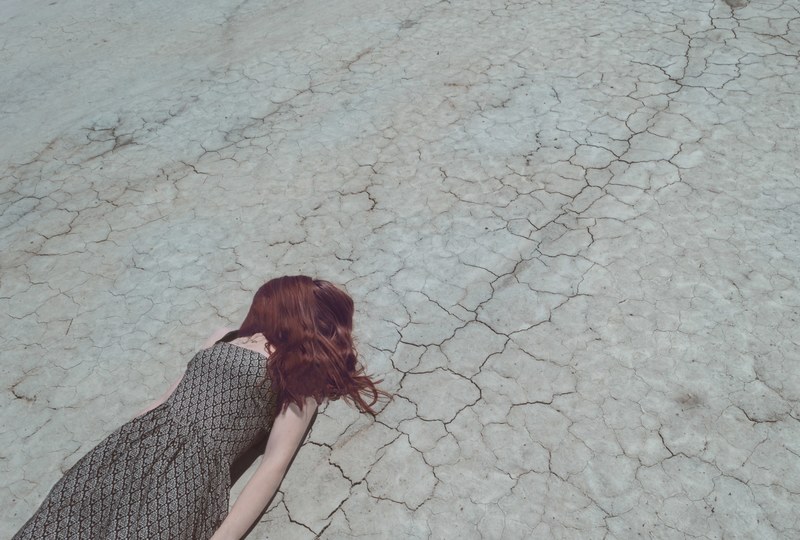 woman with hair over face lying down on cracked desert floor, exhausted from the heat 4k