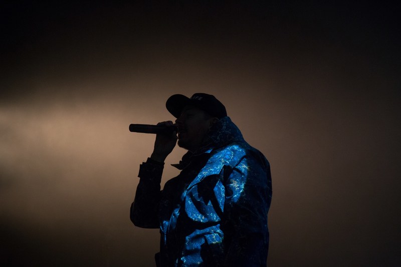 a silhouette of a musician in a cap performing with a microphone against pale smoke in the background, rapper silhouette 4k