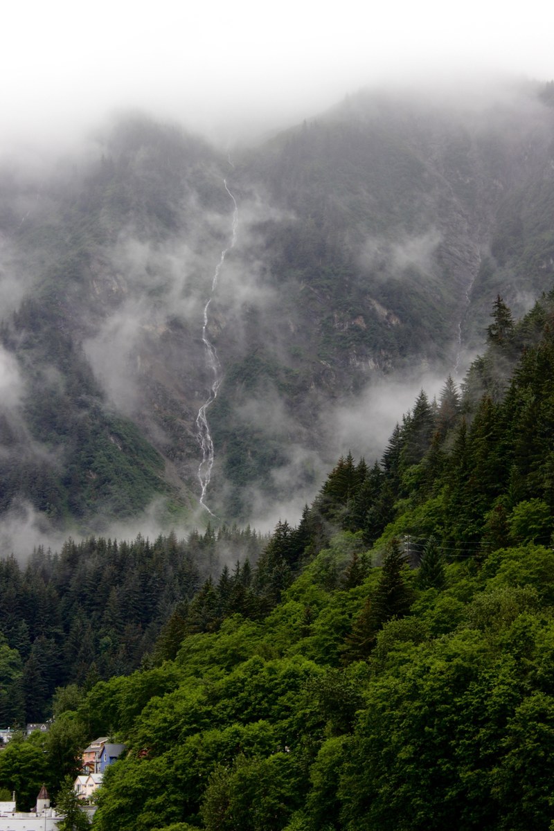 a narrow waterfall pouring down a tall mist shrouded mountain in alaska, narrow waterfall in alaska 4k