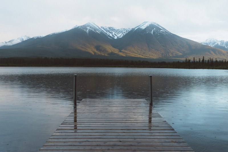 a dock over calm water that looks out to the snowcapped mountains that are reflected in the lake, mountain reflection from jetty 4k
