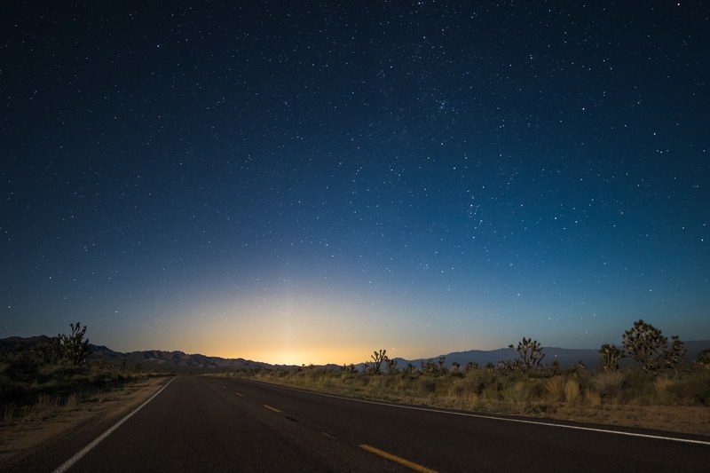 the pavement in the center of desert area leads to glowing sunrise illuminating night sky, starry sky transition at nipton 4k