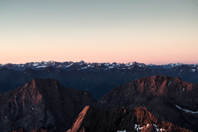 a vast mountainous area under a pale blue and red sky, mountains stretching to the horizon 4k