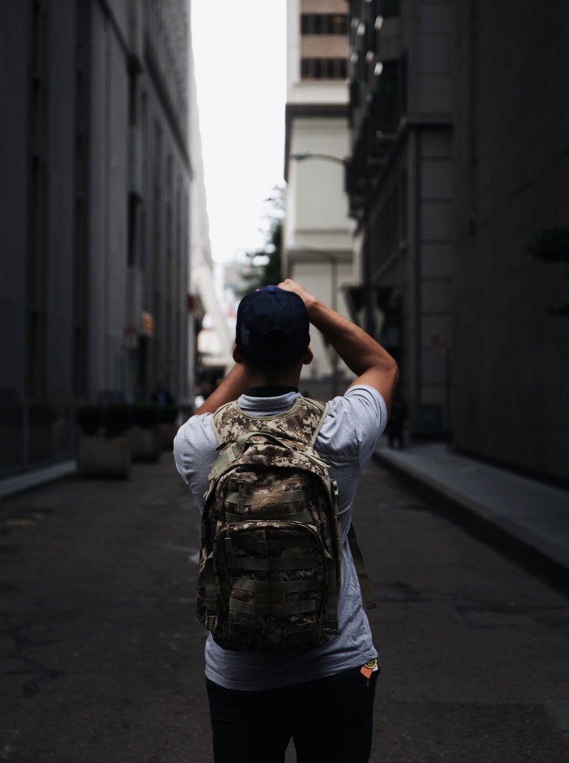 a person in a backpack faces away pointing a camera down an alleyway, person facing away with camera 4k