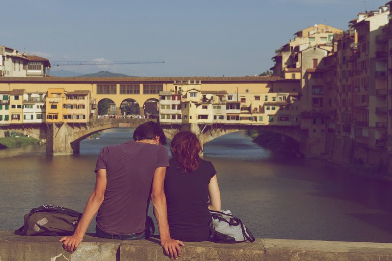 couple sitting closely together on a ledge overlooking a river, couple on bridge overlook 4k