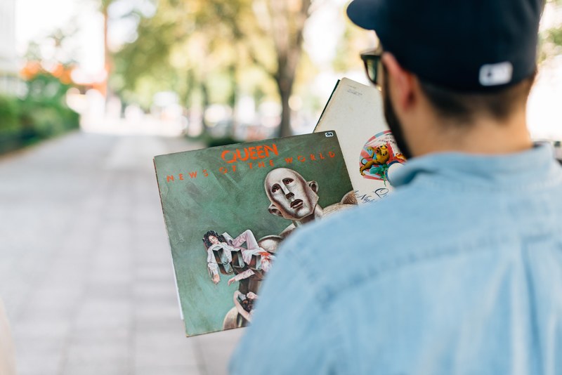 a view over the back of a man holding two queen records, man with queen vinyls 4k