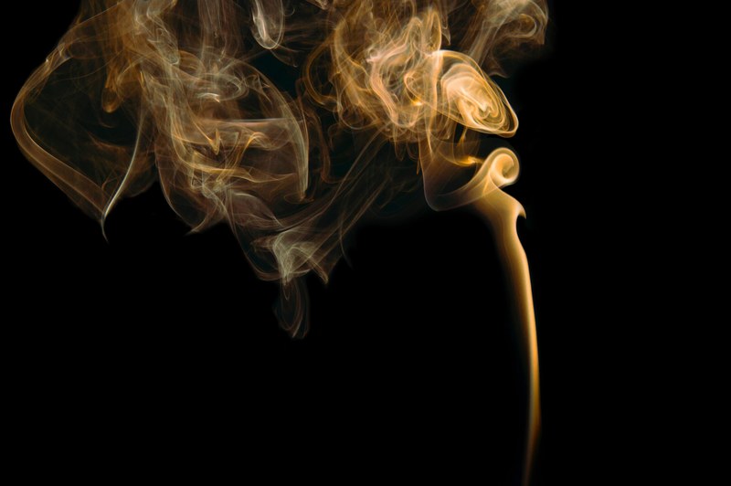 orangish yellow smoke curling into light with a black background, smoke curling into the air 4k