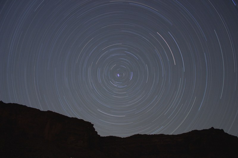concentric circles created by stars moving through the night sky over a silhouetted rock face, starry sky circle 4k