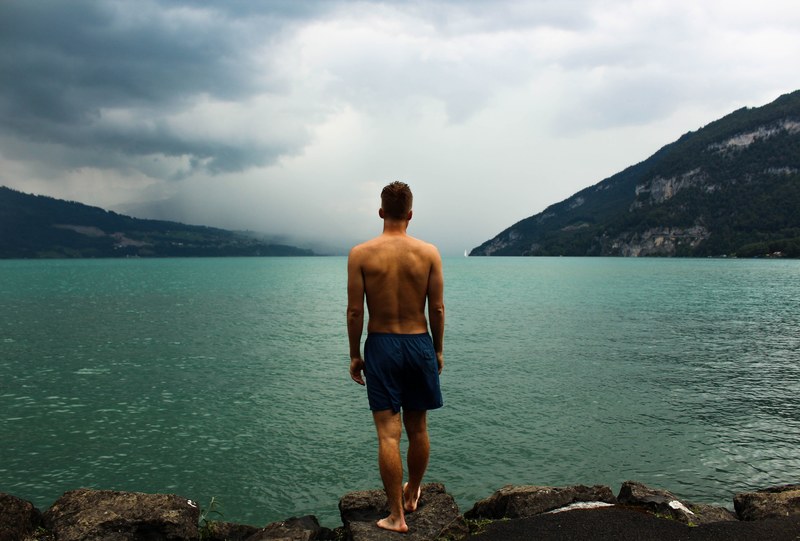 man about to take a swim in a lake by rocky bluffs, swimming at the lake 4k