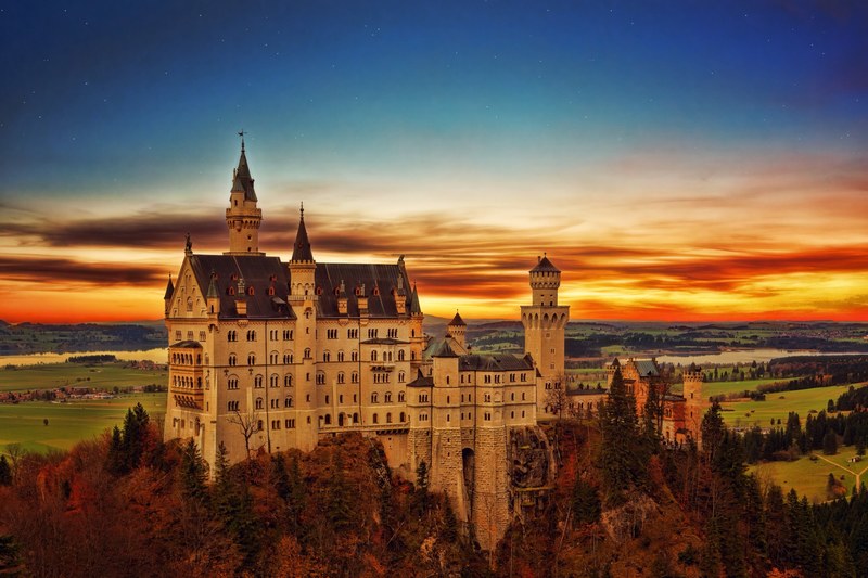 drone view of neuschwanstein castle and country landscape with orange and blue sunrise or sunset horizon, drone view castle and horizon 4k