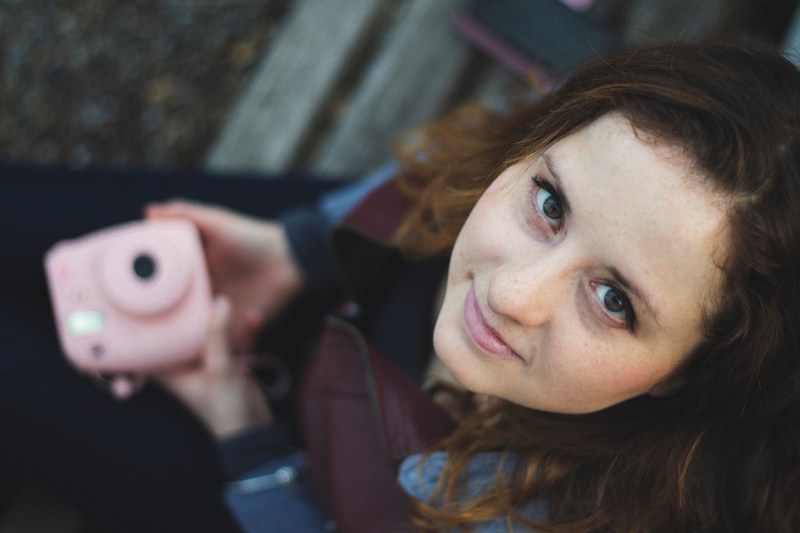 a woman holding a pink polaroid camera smiles and looks up at the camera, woman with pink camera 4k