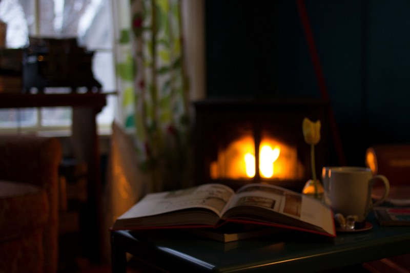 a book and coffee mug sitting on a table in a cozy den lit by firelight, cozy den 4k