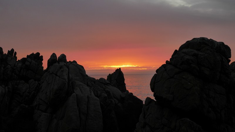 large rocks and boulders by the sea with view of the water and cloudy orange sunset between them, rock cloud sunset and ocean 4k
