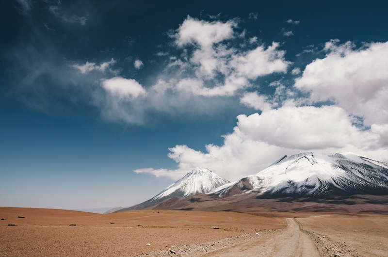 road in the plains leading to cloud covered snowy mountains in licancabur, the landscape of licancabur 4k