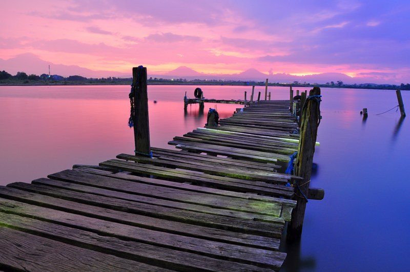 an old dock that is falling apart over the water that is reflecting the pink and purple sky, pink and purple sky over water 4k