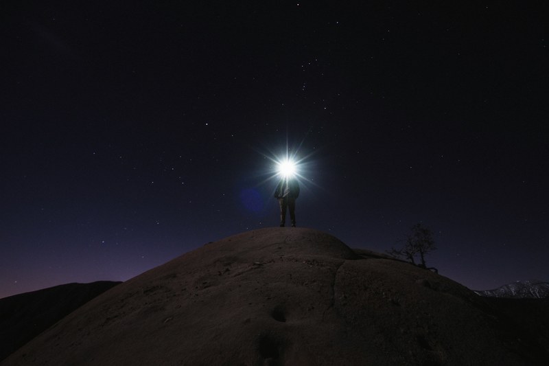 man with flashlight standing on a boulder under the starry night sky in cajon pass, stars flashlight cajon pass 4k
