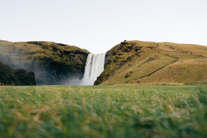 a waterfall tumbling down a mossy hill, skogafoss waterfall under white sky 4k