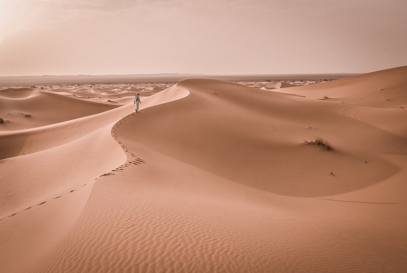 hiker walks along a sandy ridge in the desert of merzouga, adventurous desert hikes 4k