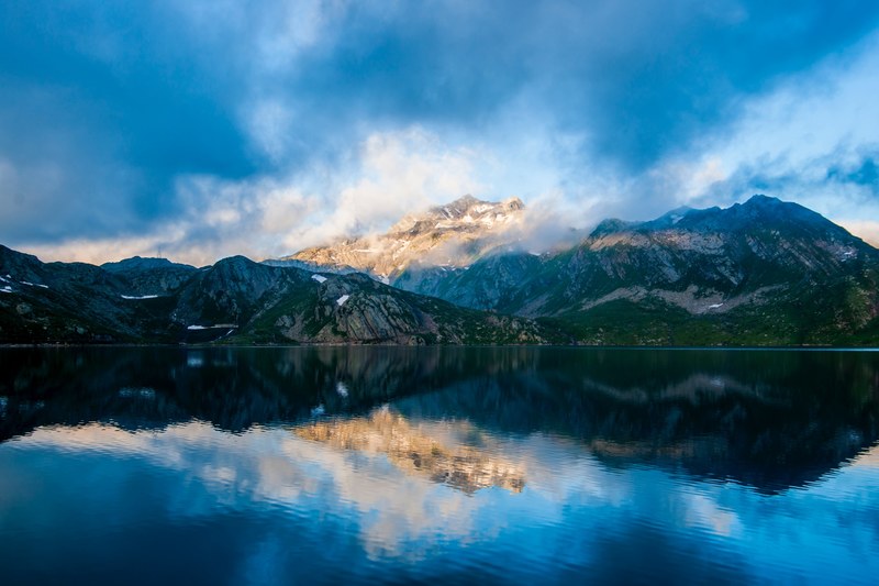 a picturesque landscape with mist shrouded mountains towering over the clear surface of a lake, misty mountains overlooking a lake 4k