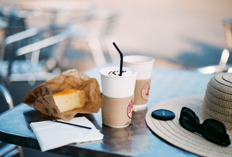 an outdoor table with iced coffee a piece of cake a hat and black sunglasses, iced coffee and cake outdoors 4k