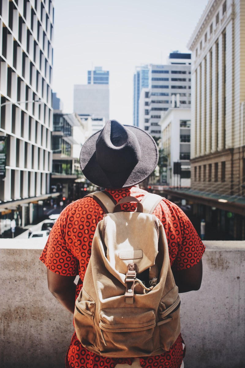 a man wearing a bright orange shirt hat and backpack looking out on the street in brisbane city, brisbane city man 4k