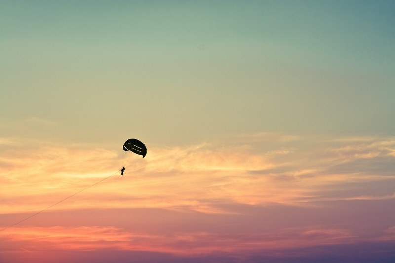 a silhouette of a paraglider in the sky during the golden hour, paragliding at dusk 4k
