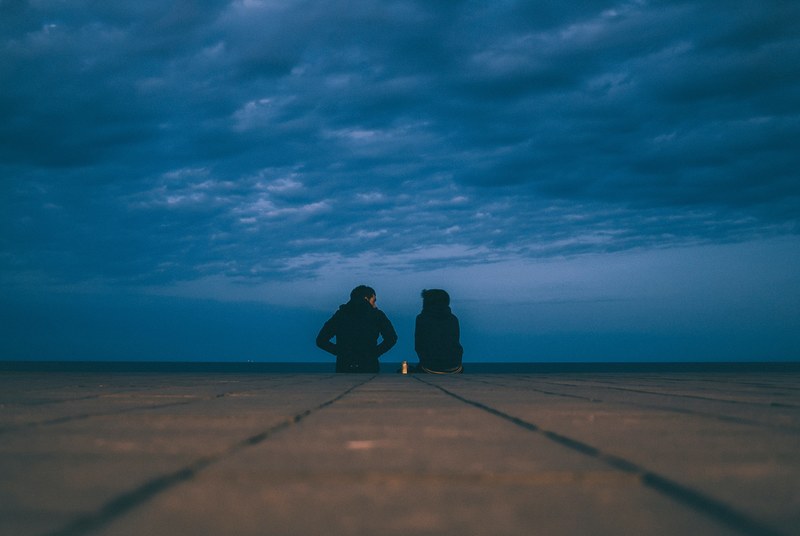 a couple sitting down under a stormy cloudy sky, stormy cloudy sky and couple 4k