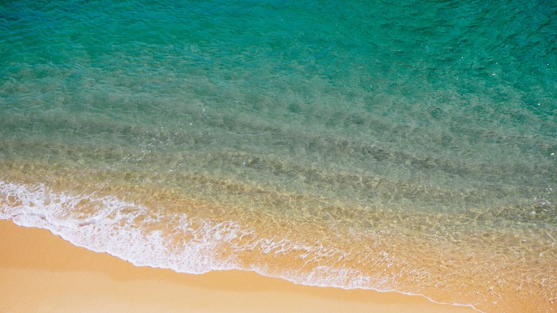 drone view of clear ocean washing on a fine sand tropical beach, ocean by sand beach drone view 4k