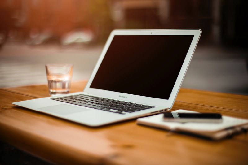 a macbook a glass of water and a notepad on a wooden table, hazy workspace 4k