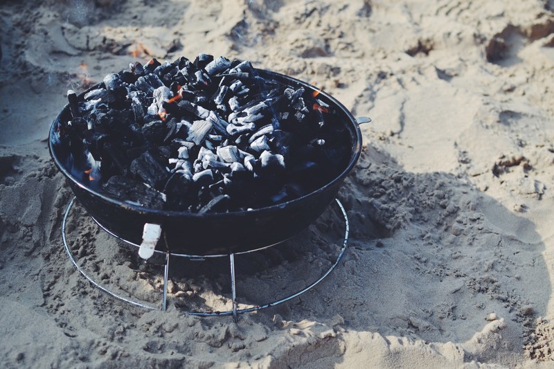 a coal bbq thats on fire at the beach, toes in the sand 4k