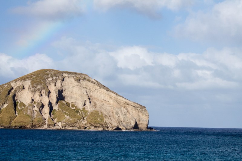a large rock hill surrounded by a cloudy sky over top of the ocean, _ocean rock hill 4k