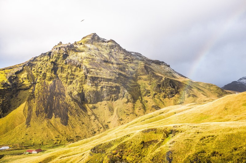 a jagged moss covered mountain with a faint rainbow to its side, rainbow near a green mountain 4k
