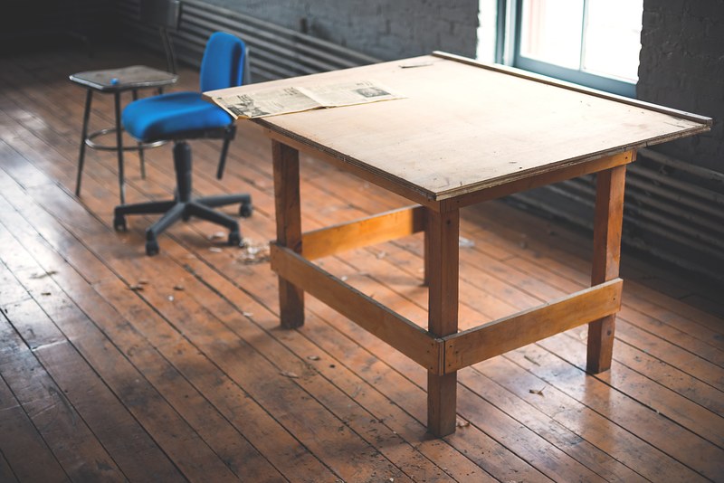 an old table near a blue office chair in a messy room, old table in a messy room 4k