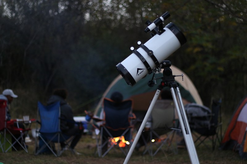 campers sitting around a campfire with their stargazing telescope set up behind them, outdoor telescope 4k