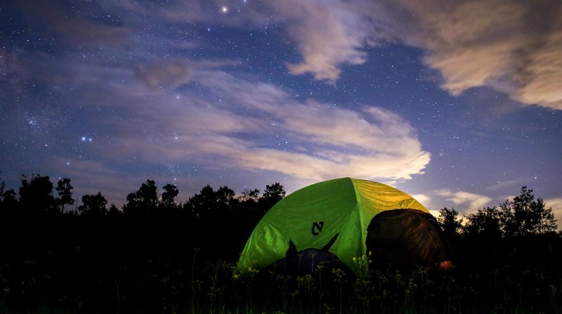 a green tent in a field under a starry sky with fluffy clouds, green tent in the evening 4k