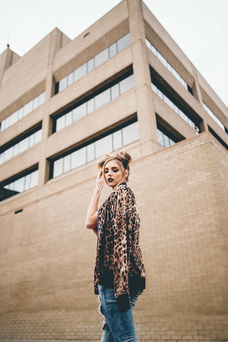a woman wearing two buns and a leopard print coat stands by a brick building, woman in two buns by building 4k