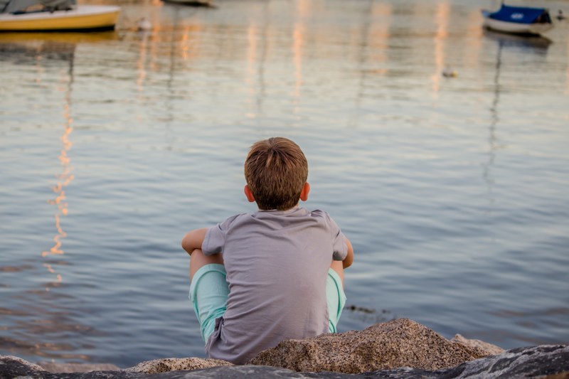 kid sitting alone near a lake thinking, childhood reflection 4k