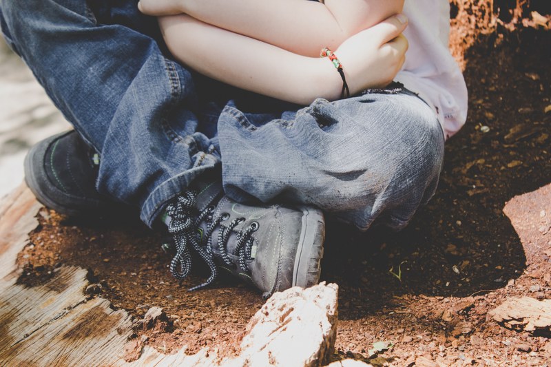 a child in jeans boots and a bracelet sits on dirt crossing their legs, child crossing their legs 4k