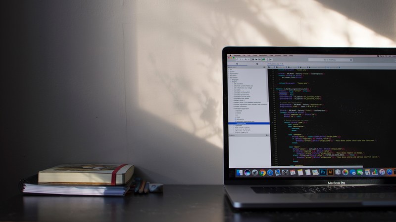 two books on a desk near a macbook with lines of code on its screen, light work 4k