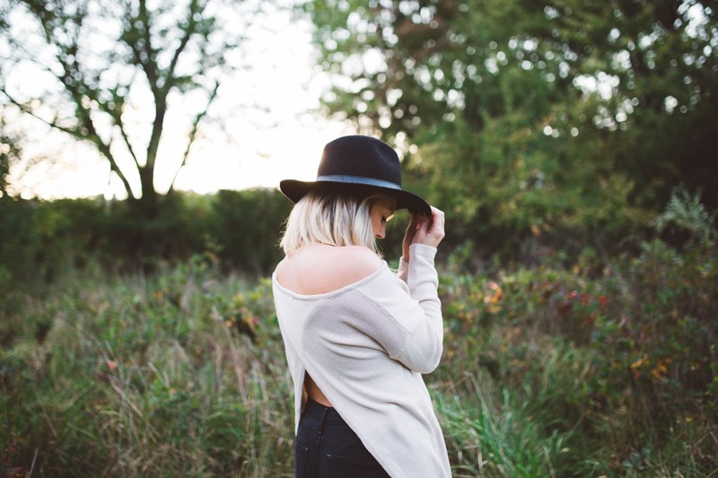 a blonde woman holding the brim of her black hat in a meadow, woman in black hat on a meadow 4k