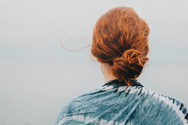 woman with red hair wearing a tie dye blue shirt facing away from camera and looking at gray sky, woman red hair looking at sky 4k