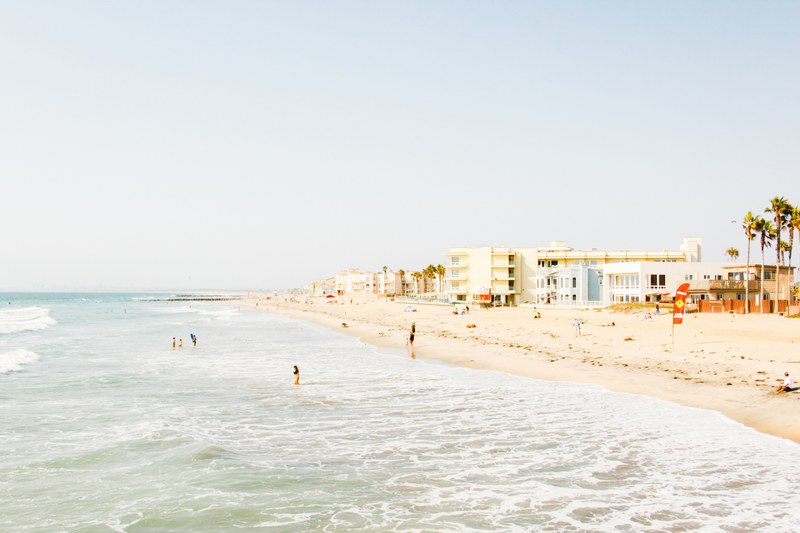 a few people walking on the beach and swimming in the sea with holiday resorts at the back, quiet holiday beach 4k