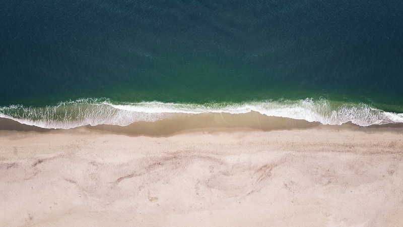 an aerial view of waves crashing on an empty beach, calm 4k