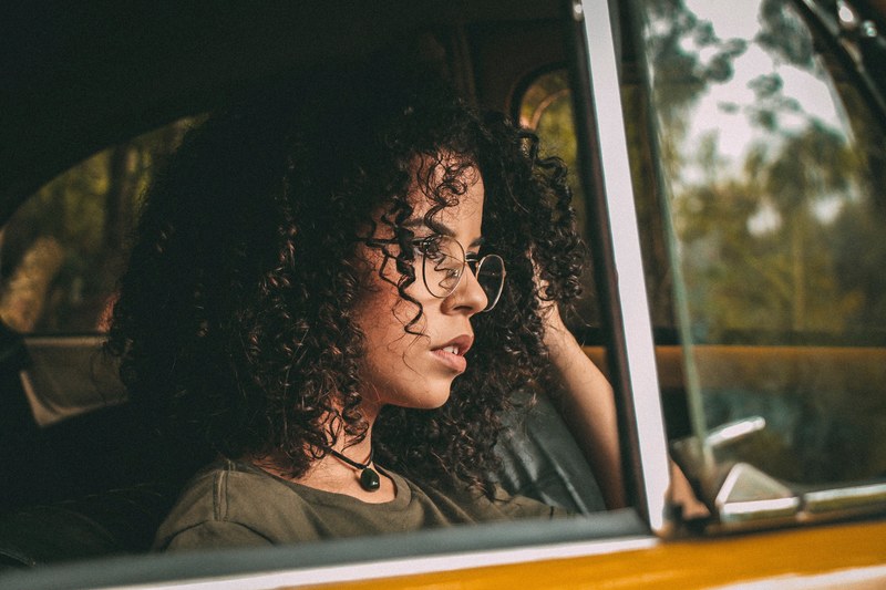 woman with curly hair and vintage glasses staring out a car window, looking out the car window 4k