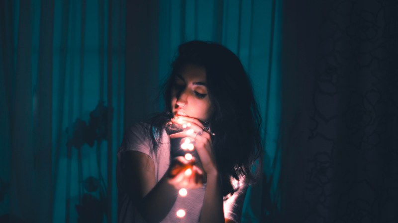 young woman strings fairy lights in a dimly lit blue room, quiet moments 4k