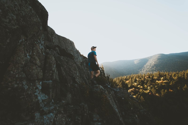 a young man in a cap on a jagged rock formation in a morning, hiking on rugged rocks 4k