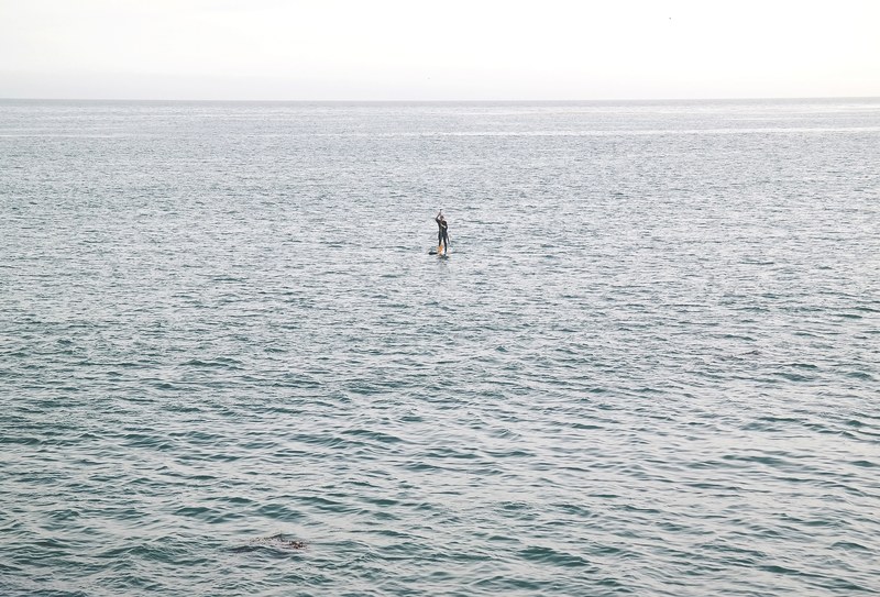 a distant shot of a paddle boarder in a huge mass of tranquil sea, paddle boarder finds solitude in the sea 4k